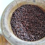 A close-up of roasted coffee beans in a rustic wooden bowl, highlighting texture and color.