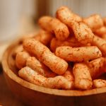 A close-up shot of crunchy, spicy snack sticks in a wooden bowl on a table.