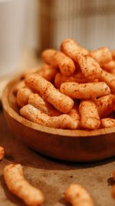 A close-up shot of crunchy, spicy snack sticks in a wooden bowl on a table.