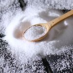 A close-up view of coarse sea salt on a dark surface with a wooden spoon.