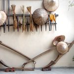A display of traditional Vietnamese hats and farming tools against a wooden rack on a white wall.