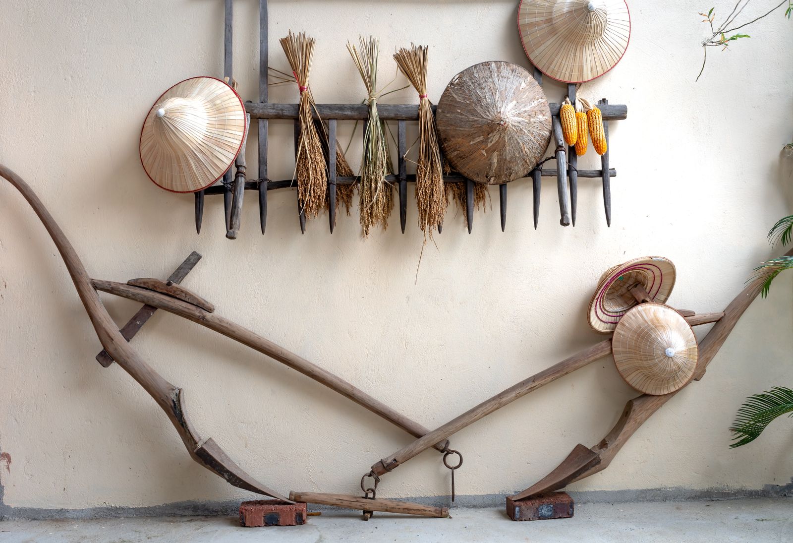 A display of traditional Vietnamese hats and farming tools against a wooden rack on a white wall.