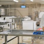 A factory worker in uniform measures ingredients on a digital scale in an industrial setting.