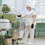 A food industry worker in a modern kitchen using an industrial mixer with protective gear.