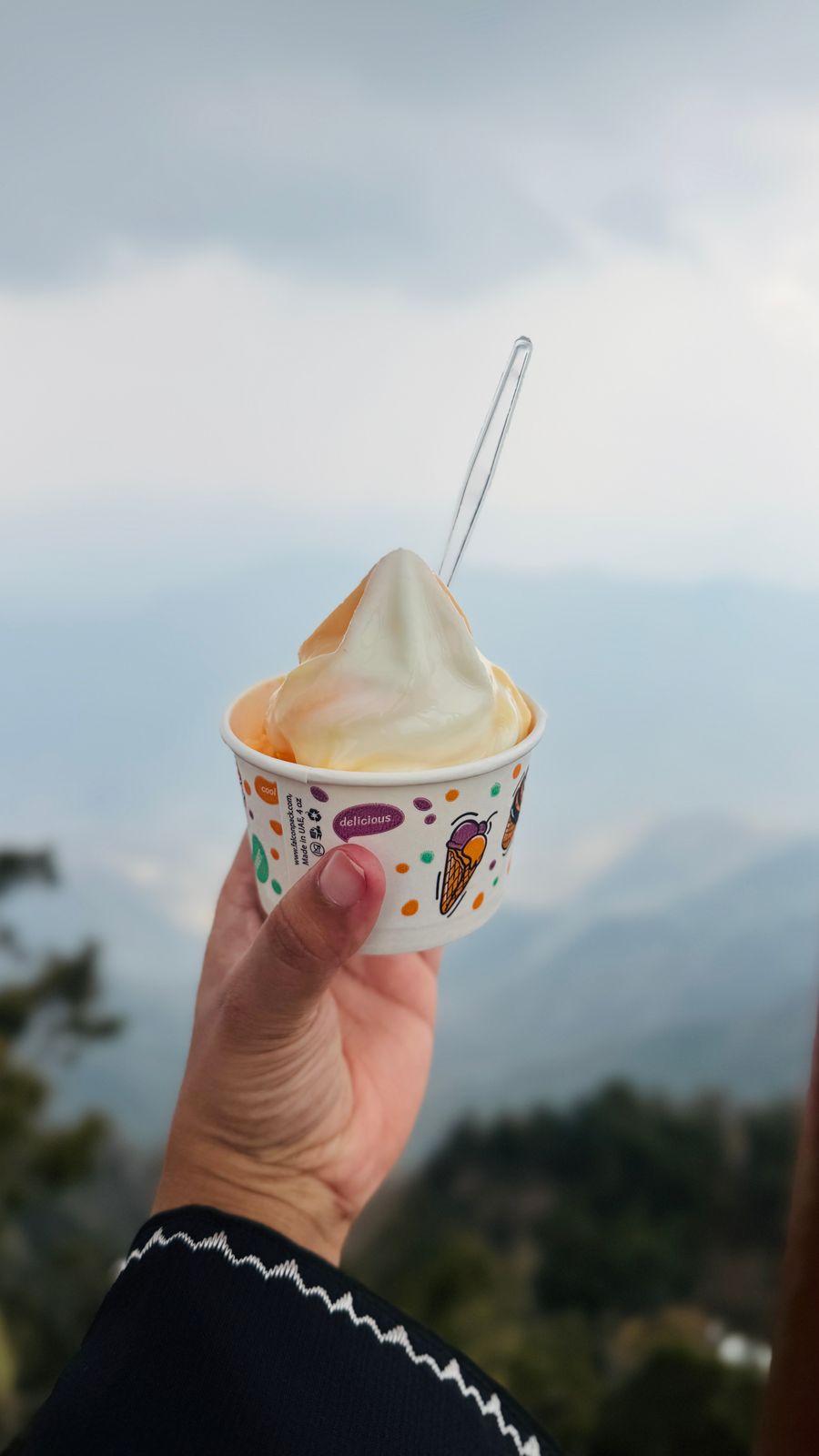 A hand holding ice cream with mountains in the background, creating a refreshing outdoor scene.