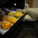 A warm, inviting scene of fresh biscuits being taken out of the oven with an oven mitt.