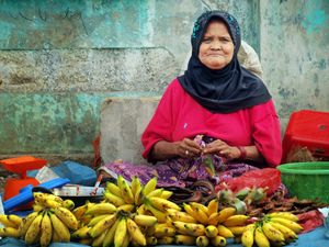 An elderly woman selling fresh bananas at a traditional market in North Sumatra, Indonesia.