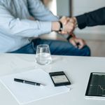 Business meeting with handshake and financial analysis displayed on a tablet.