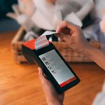 Close-up of a cashless payment transaction using a modern payment terminal indoors with a floral background.
