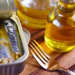 Close-up of canned sardines in olive oil with a fork on a wooden surface.
