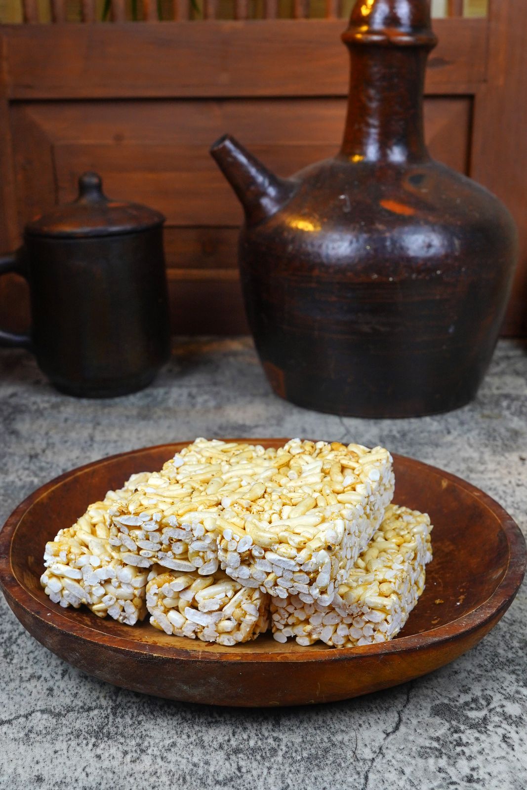 Close-up of traditional puffed rice cakes on a rustic wooden plate against rustic pottery in a cozy setting.