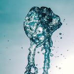 Close-up of water splash in mid-air against a bright sky, capturing motion and transparency.