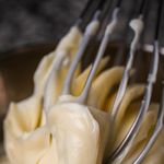 Close-up view of a whisk mixing creamy cake batter in a bowl, highlighting texture.