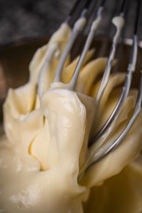 Close-up view of a whisk mixing creamy cake batter in a bowl, highlighting texture.