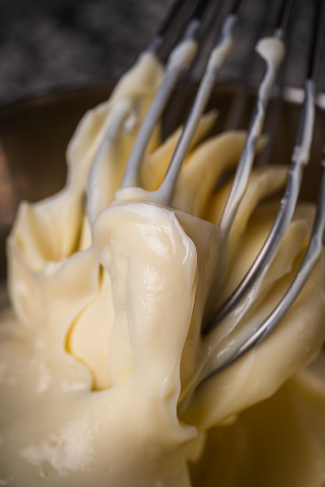 Close-up view of a whisk mixing creamy cake batter in a bowl, highlighting texture.