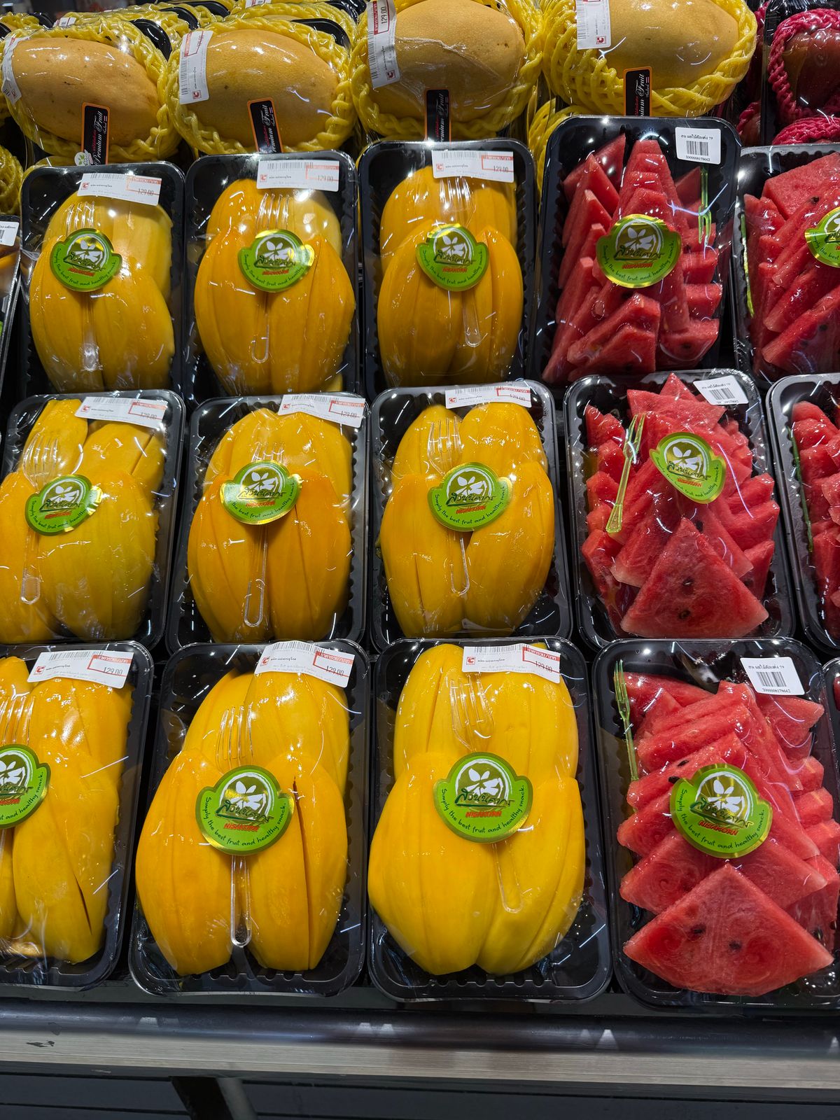 Colorful display of packaged mango and watermelon slices in a market setting.