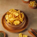 Crispy corn chips in a wooden bowl with cheese, corn, and herbs.