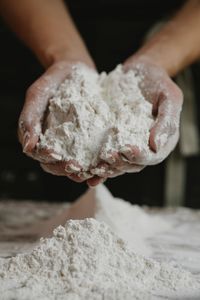 Crop anonymous female preparing and showing white clean flour in hands in kitchen
