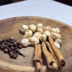 Detailed view of spices including cloves, cardamom, and cinnamon on a wooden plate.