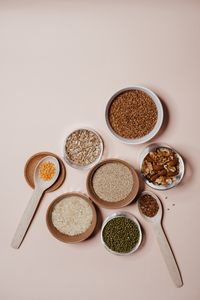 Flat lay of various grains and nuts in bowls and wooden spoons on neutral background.