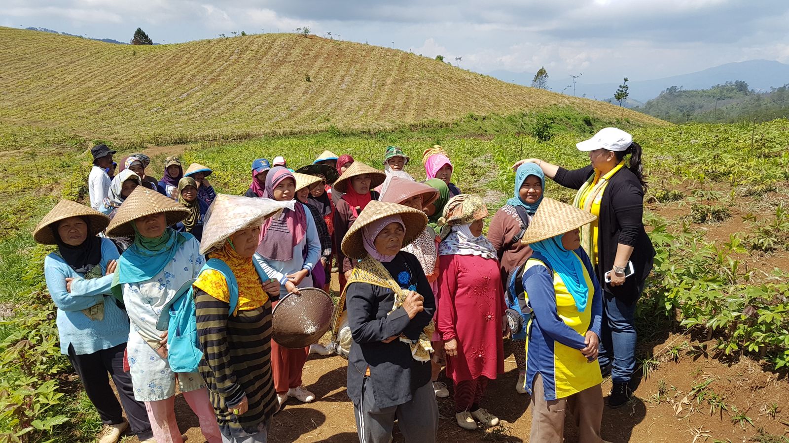 Group of women farmers wearing traditional hats gathered on a sunny field, showcasing rural life.
