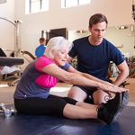 Imgi 161 senior woman exercising in gym being encouraged by ADB54EP