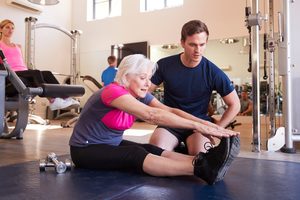 Imgi 161 senior woman exercising in gym being encouraged by ADB54EP