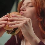 Imgi 171 happy hungry caucasian woman female girl client customer eat chew tasty burger eating delicious juicy hamburger enjoy chewing cheeseburger indoo