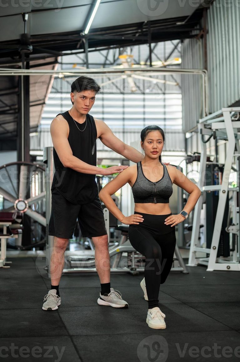 Imgi 195 a professional asian male fitness coach is training a female client in a gym checking her form photo