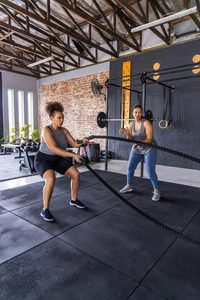 Imgi 495 diverse female workout partners wearing athletic clothing using battle ropes rubber mat gym rope teamwork training strength