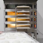 Industrial bakery scene with dough preparation and multi-shelf oven heating.