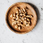 Overhead shot of peeled peanuts served on a rustic wooden plate against a marble background.