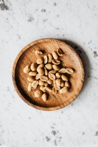 Overhead shot of peeled peanuts served on a rustic wooden plate against a marble background.