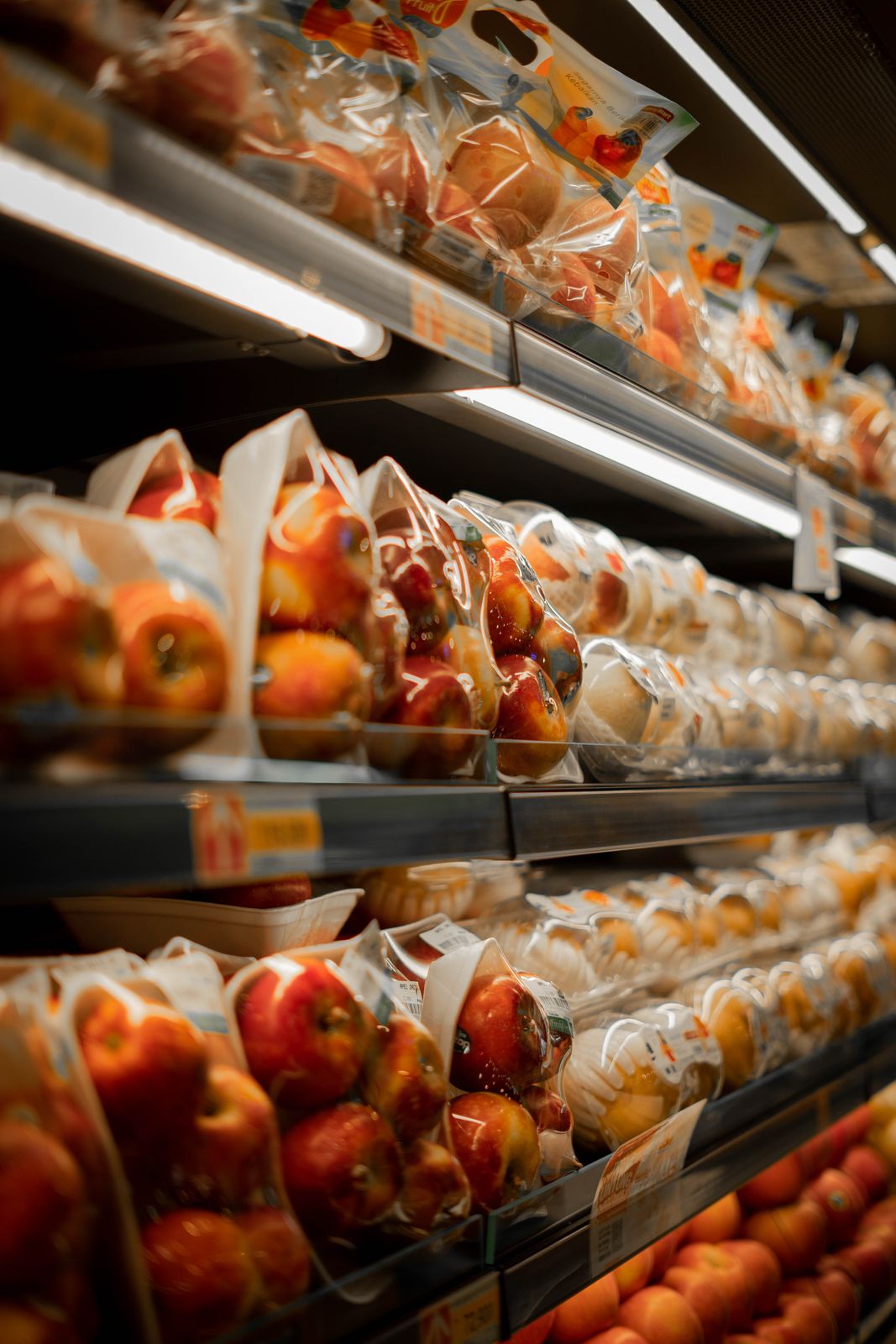 Packaged fresh apples displayed on a supermarket shelf with bright lighting.