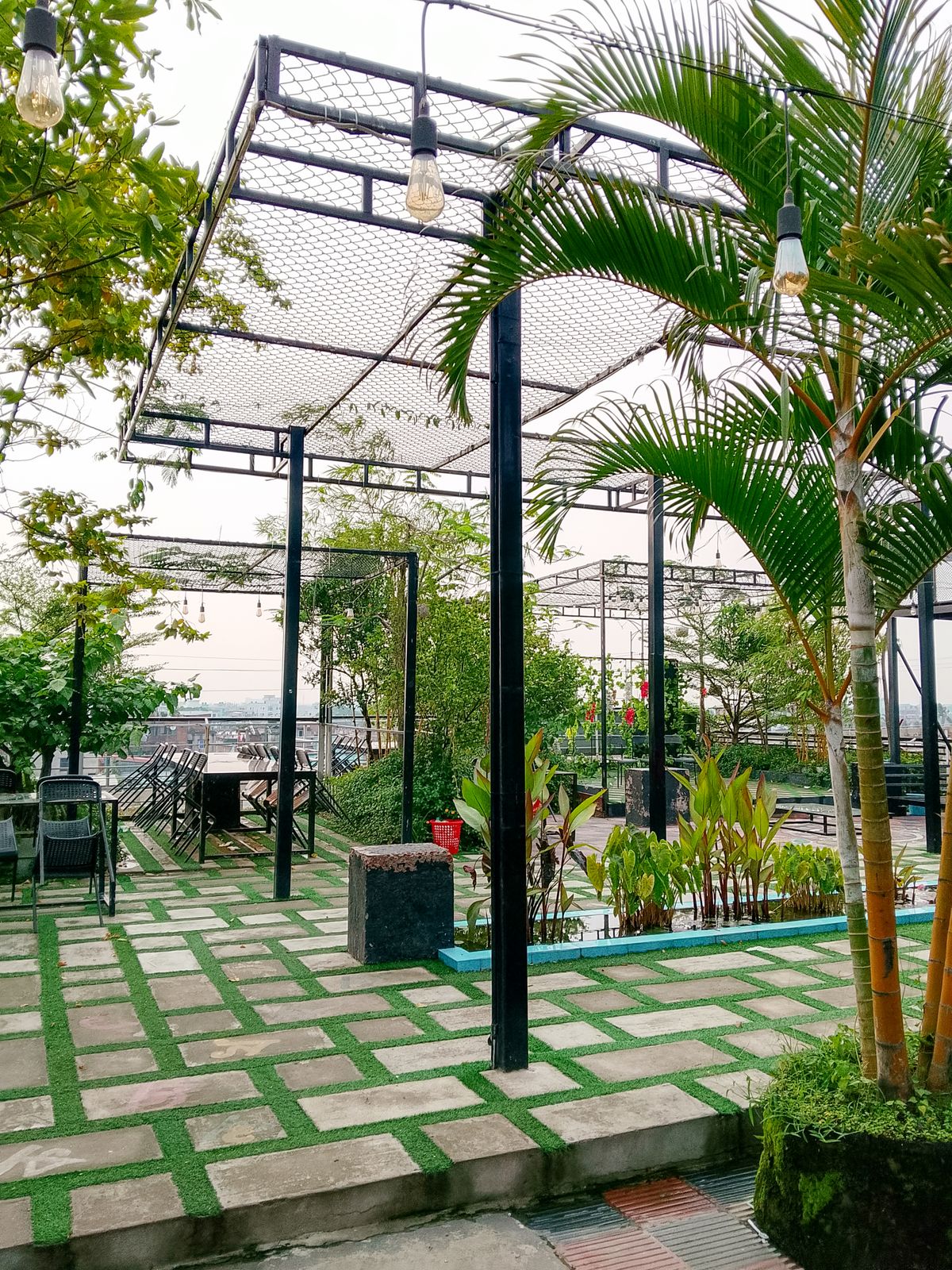 Spacious outdoor patio with lush greenery, pergolas, and vintage lighting, perfect for relaxation.