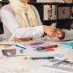 Two business professionals shaking hands over financial documents in an office setting.