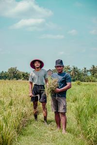 Two farmers in hats working in a vibrant green field on a sunny summer day.