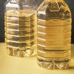 Two large recyclable plastic bottles filled with cooking oil on a yellow surface.
