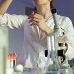 Young scientist in a laboratory carefully inspecting a sample, surrounded by lab equipment.