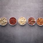 Flat lay of assorted nuts in bowls on a textured gray surface, highlighting healthy food options.