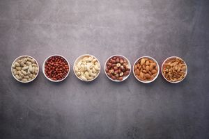 Flat lay of assorted nuts in bowls on a textured gray surface, highlighting healthy food options.